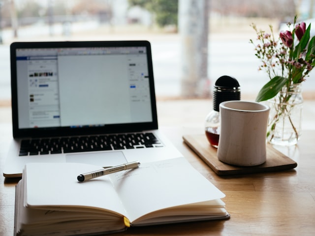 Desk set up with a laptop, open notebook and pen, and coffee cup